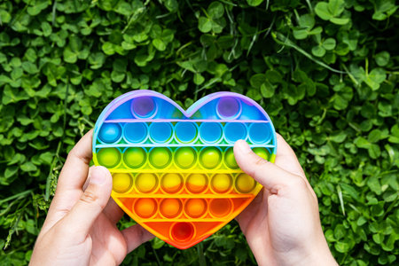 Child plays on the grass with a simple dimple relaxing toy. Pop it toy heart shaped, rainbow colored...