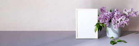 Mock up photo frame in minimalistic interior. Modern still life scene of white frame and bouquet of lilacs. Concept trendy home decor. Banner in pastel colors.の写真素材