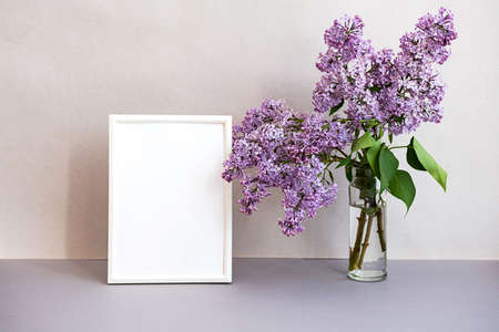 Mock up photo frame in minimalistic interior. Modern still life scene of white frame and bouquet of lilacs. Concept trendy home decor. Banner in pastel colors.の写真素材