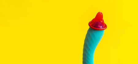 Sex toy blue dildo vibrator and red condom, on the yellow desk, copy space, close-up. Modern concept of safe sex, or sex education.の写真素材