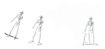Toy skeletons with skateboards and scooter. Creative composition with rider skeleton on the white background. Minimalism stile, copy space.の写真素材