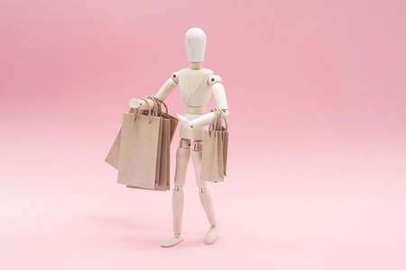 Sale or shopping concept, in minimalism style. Wooden puppet with craft paper shopping bags, on the pink background.の写真素材