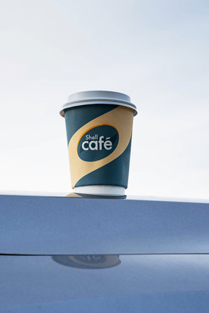 Kemerovo, Russia - 03 October 2021: Shell Cafe to go coffee cup stands on the car hood. Paper cup from Shell Cafe takeaway.のeditorial素材