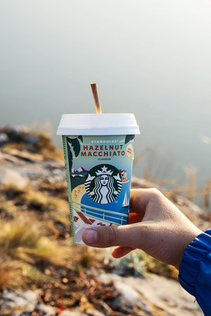 Kemerovo, Russia - 17 October 2021: Man hold Starbucks coffee on scenic nature background. Hazelnut macchiato to go coffee cup, close-up.のeditorial素材