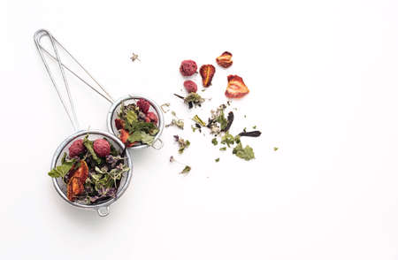 Dried tea leaves and berries in tea strainer. Composition with organic, natural herbal tea and dry berry on white desk.の写真素材
