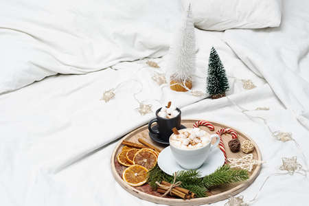 Christmas morning coffee cups with marshmallows in bed, candy cane, christmas decoration. Cozy home, winter holiday mood.の写真素材