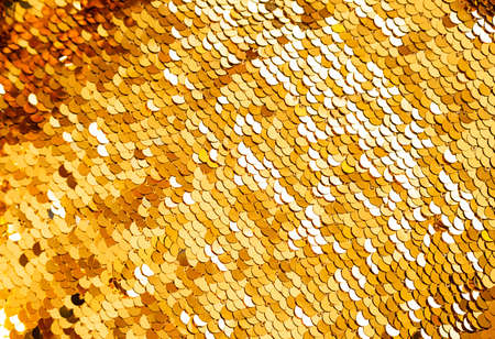 Golden sequins macro background. Sparkling sequined textile. Abstract texture scales with shiny sequins on fabric.の写真素材