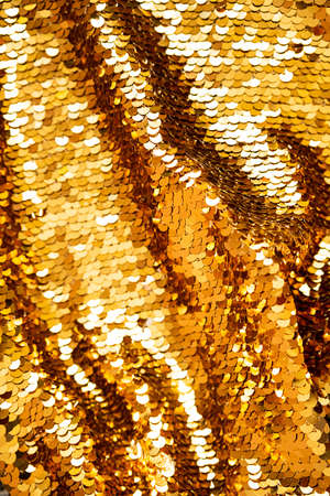 Golden sequins macro background. Sparkling sequined textile. Abstract texture scales with shiny sequins on fabric.の写真素材