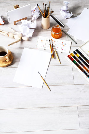 Watercolour, stack of paper, paintbrushes and other artistic equipment on floor at home. Home...