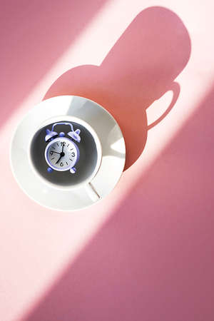Violet vintage alarm clock in coffee cup on pastel pink background. Breakfast time concept, morning, activity, daily routine.の写真素材