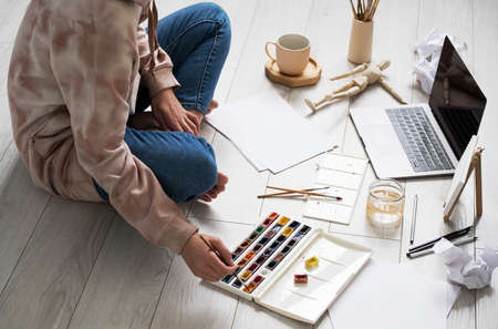 Woman painting on canvas, sitting on floor at home. Home tutoring, education, hobby or leisure concept.の写真素材