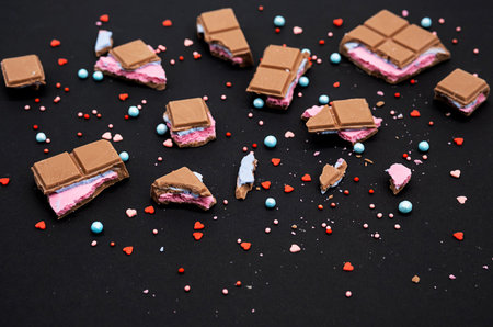 Broken pieces chocolate bar on black. Crumbled chocolate bar with pink blue filling of various size pieces, close up.の写真素材