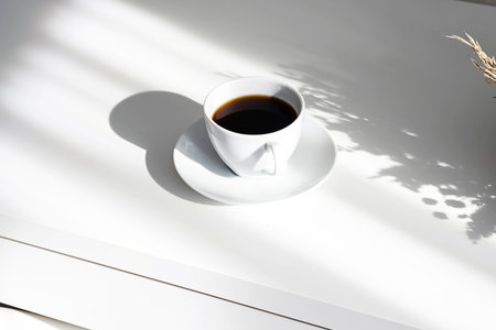 Aromatic black coffee cup on white table with interesting shadows.Scandinavian style, still life in...