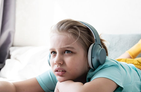 Child wearing headphones listens to music. Cute boy listening to music in earphones lying on bed.