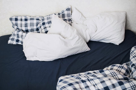 Rumpled bedding after sleep. Pillows, sheets and blanket, close up.の写真素材