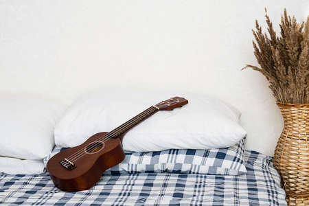 Ukulele guitar resting on bed. Hawaiian acoustic guitar in bedroom.の写真素材