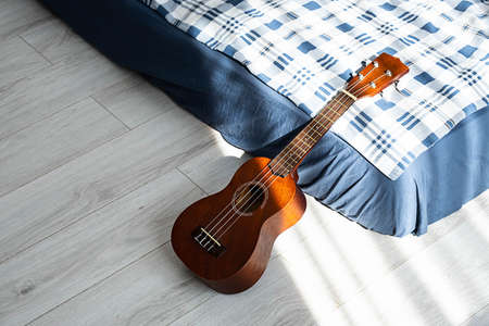 Ukulele guitar resting on bed in sunlight, close up. Hawaiian acoustic guitar in bedroom.の写真素材