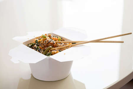 Rice with pork and vegetables in take-out box with chopsticks on table. Yummy Chinese wok from takeaway.の写真素材