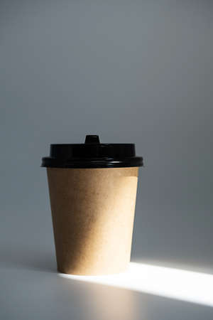 Mock up disposable craft cardboard takeaway coffee cup in light beam. Template to go coffee cup against grey background.の写真素材