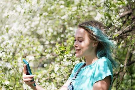 Blue haired woman taken selfie against spring blossom tree.