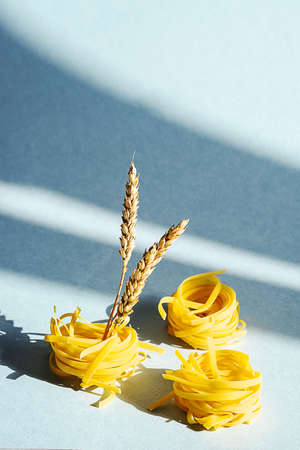 Uncooked pasta nest and ears of wheat. Creative composition of raw pasta on blue background.の写真素材