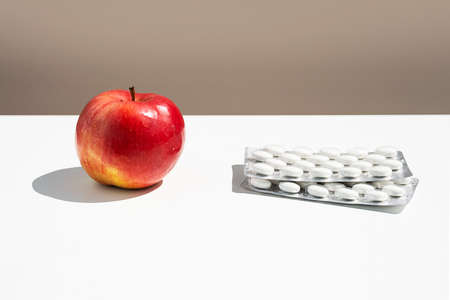 Red apple and pills or vitamin capsules on white table, copy space. Wellness, diet or supports for health concept.の写真素材