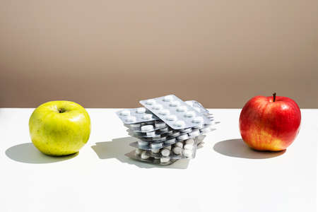 Apples and pills or vitamin capsules on white table, copy space. Wellness, diet or supports for health concept.の写真素材