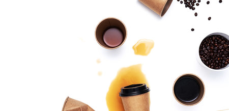 Disposable coffee cups, roasted coffee beans and spilling coffee on white table. Creative still life, copy space.の写真素材