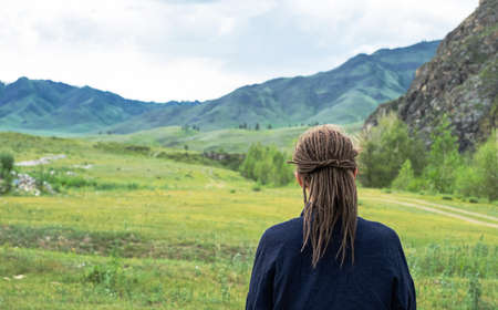 Dreadlocks woman looking at mountain range. Rear view of hipster tourist woman. Travel freedom concept.の写真素材