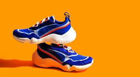Blue sneakers on orange background. Trendy sport shoe, street casual footwear.