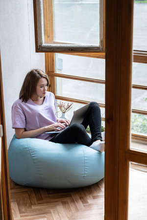 Young woman using laptop on sunny balcony. Working at home, freelance concept.