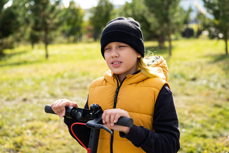 Boy rides an electric scooter in autumn park. Schoolboy using e-scooter at sunny day.の写真素材