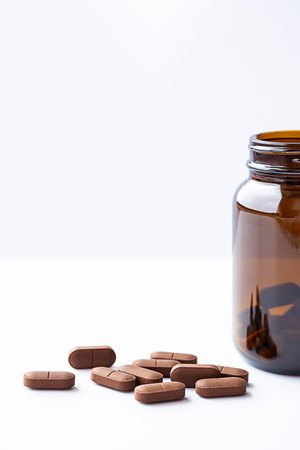 Vitamin capsules spilling pills out from medicine amber glass bottle on white. Natural supplement for wellness, treatment and support for health.の写真素材