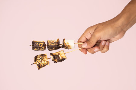 Hand holding toasted marshmallows on skewers.の写真素材