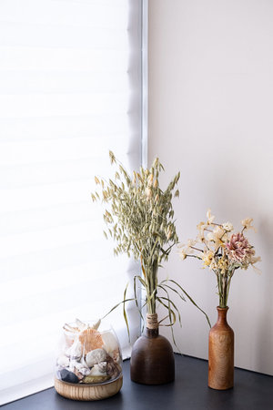 Dried floral arrangement and seashells in rustic vases on windowsill by window.の写真素材