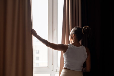 Woman opening curtains in sunlit room. Concept of morning routine.の写真素材