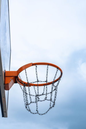 Outdoor basketball hoop with chain net against cloudy sky.