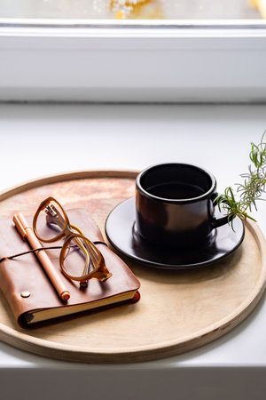 Cozy workspace with notebook, glasses and coffee cup on wooden tray.の写真素材