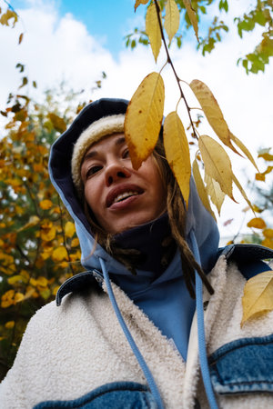 Woman in autumn attire smiling under yellow leaves on sunny day. Enjoying fall outdoors concept.の写真素材