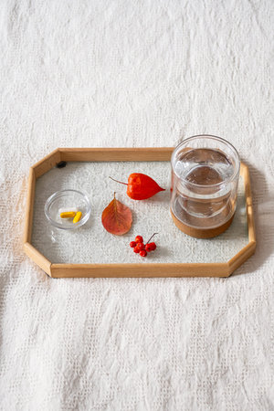 Glass of water, dietary supplement dose and autumn leaves on tray. Seasonal vitamin deficiency...
