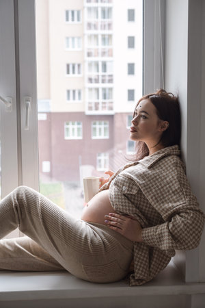 Pregnant woman enjoying a cup of coffee by the window.の写真素材