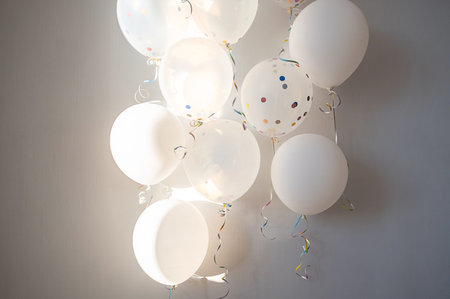 White balloons with ribbons floating against light wall. Festive and celebratory mood.