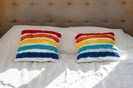 Rainbow colored pillows on white bed in natural sunlight. Cozy and cheerful decorの写真素材