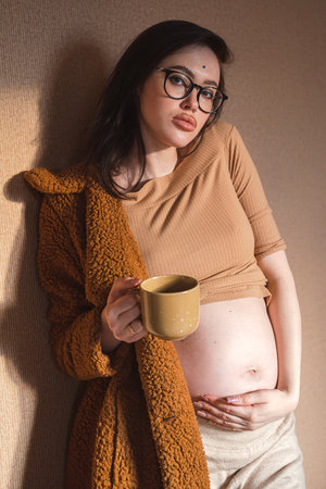 Pregnant woman holding her belly and drinking tea from mug.の写真素材
