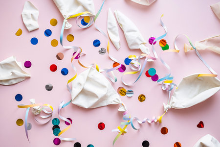 Deflated balloons and colorful confetti scattered on pink.の写真素材