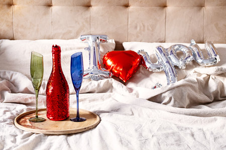 Champange bottle, two glasses and "I love you" balloon on the bed. Romantic concept.の写真素材