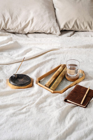 Incense Stick with Smoke, Glass of Water and Notebook on Bed. Morning Ritual Scene.