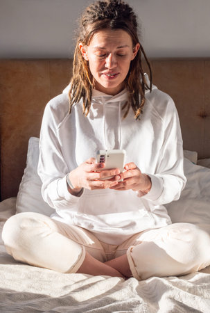 Woman Using Smartphone on Sunlit Bed. Relaxation and Modern Lifestyle.