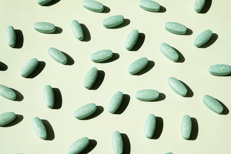 Vitamin Pills Scattered on Green Background. Medication and Pharmacy for Healthcare and Wellness Concept.の写真素材