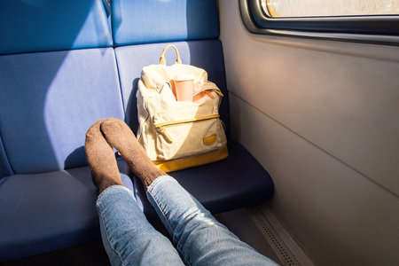 Travelers Enjoy a Comfortable Moment Inside a Train Cabin, with Feet Resting on Seat and Backpack Nearby.の写真素材